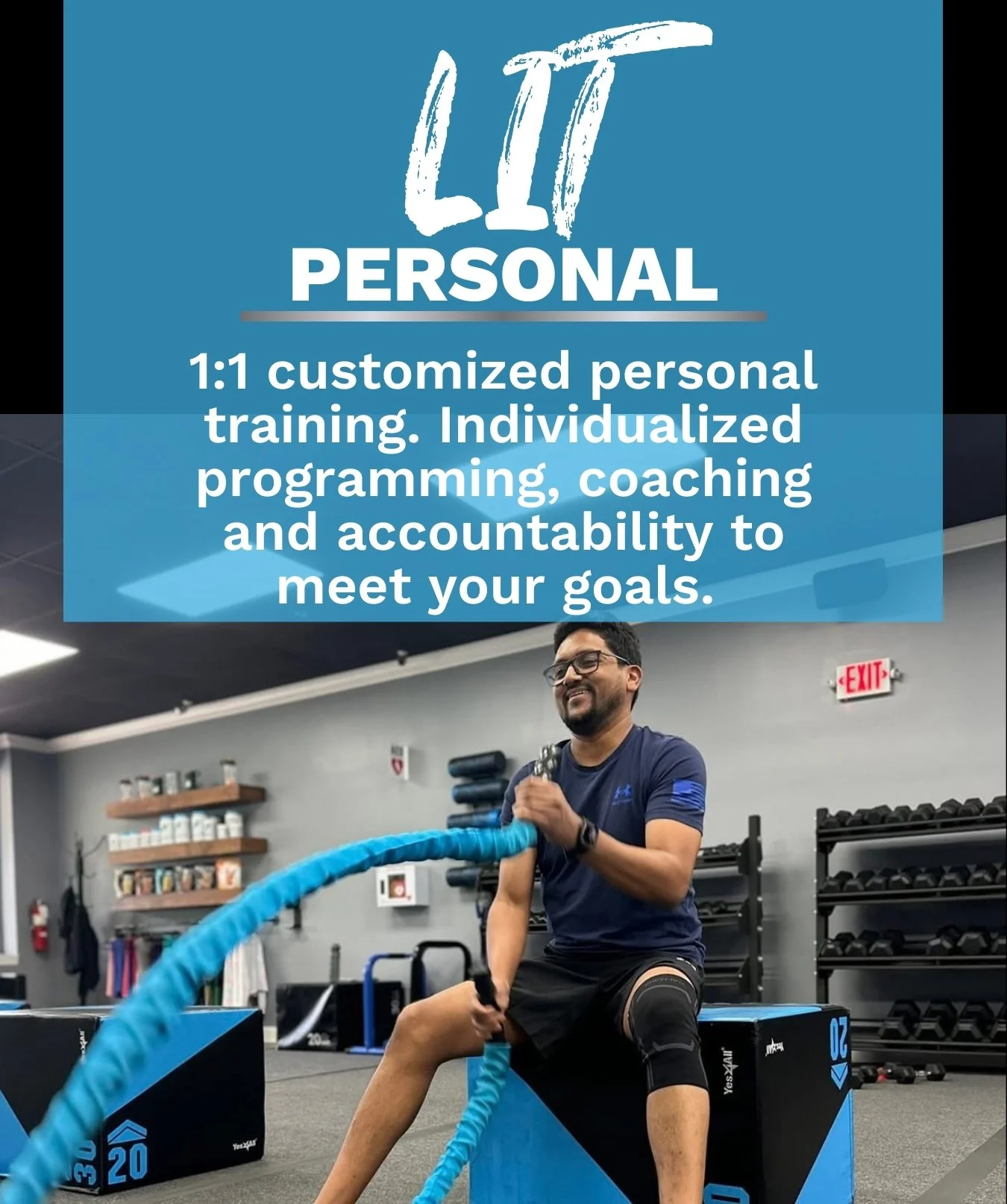 A man exercising in a gym, sitting on a blue plyometric box with a smile, holding battle ropes, with gym equipment and a wall with shelves in the background.