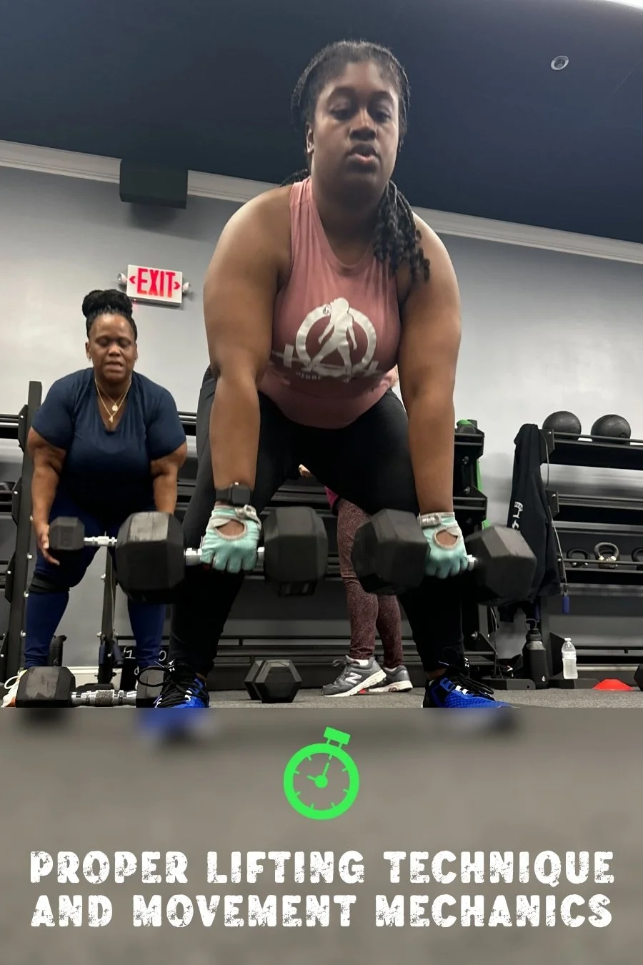 Woman with black braided hair, wearing a pink tank top and black leggings, performing a deadlift with dumbbells in a gym. Behind her, another woman with black hair in a bun, wearing a navy shirt, is observing or coaching. The gym has black shelves with weights and fitness accessories. Text overlay states "Proper lifting technique and movement mechanics" with a green stopwatch icon.