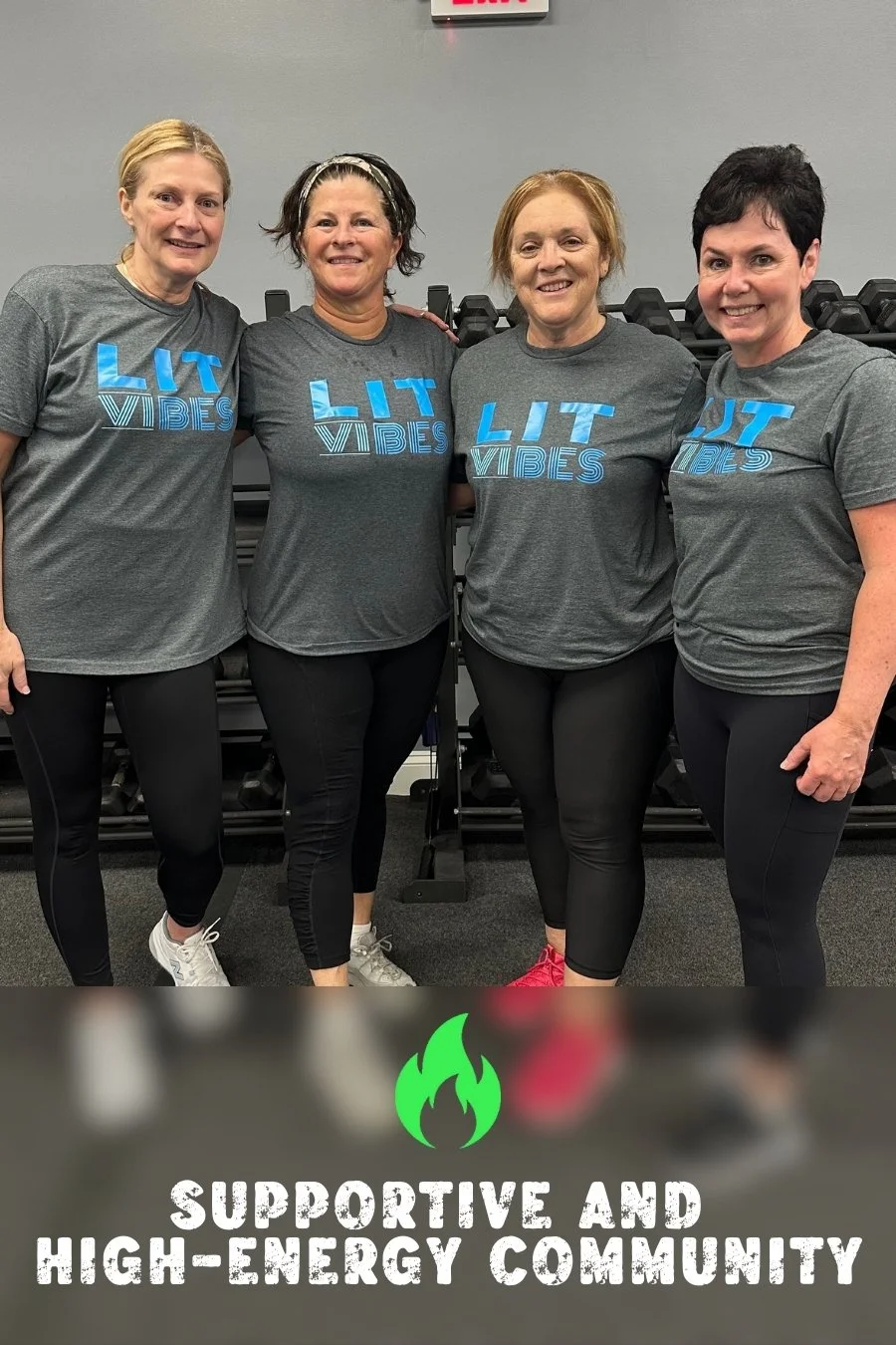 Four women standing together in workout gear, smiling, in a gym with dumbbells in the background, wearing matching 'LIT VIBES' t-shirts.