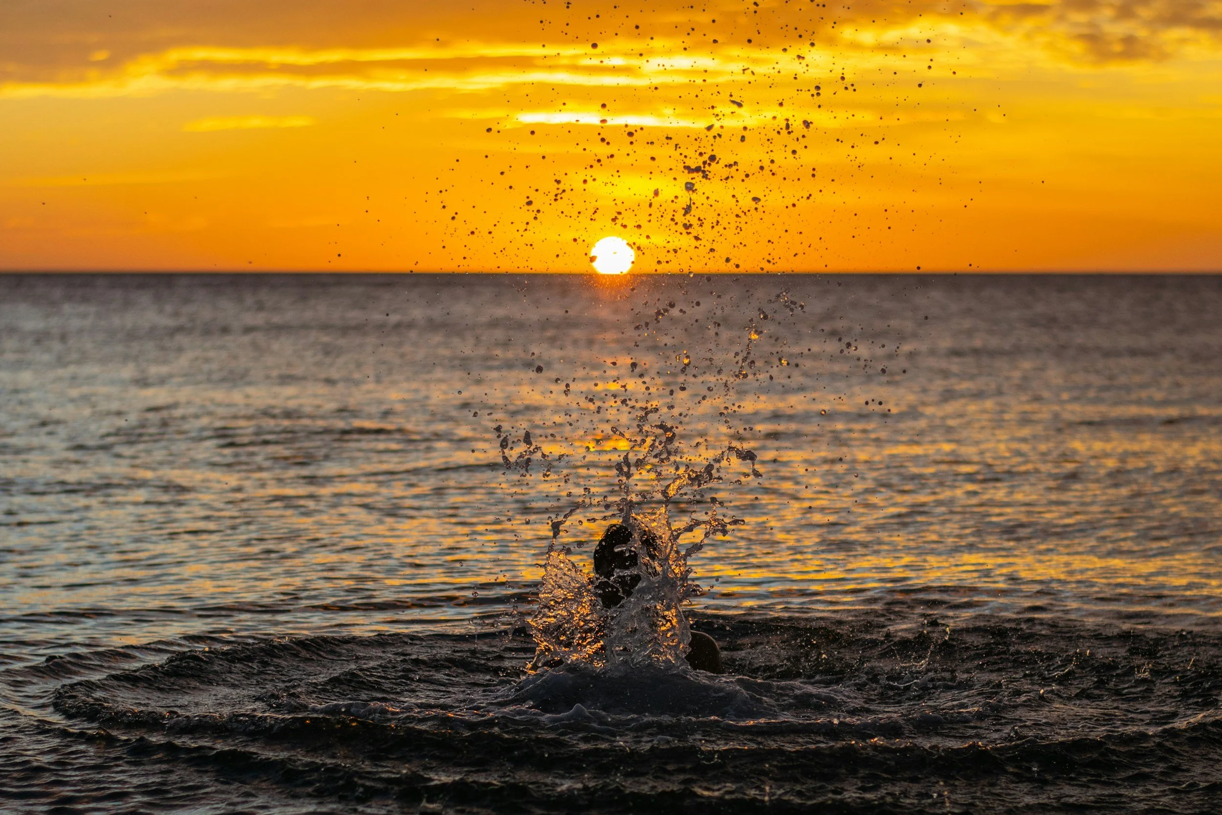 Sunset over the ocean with a splash of water in the foreground