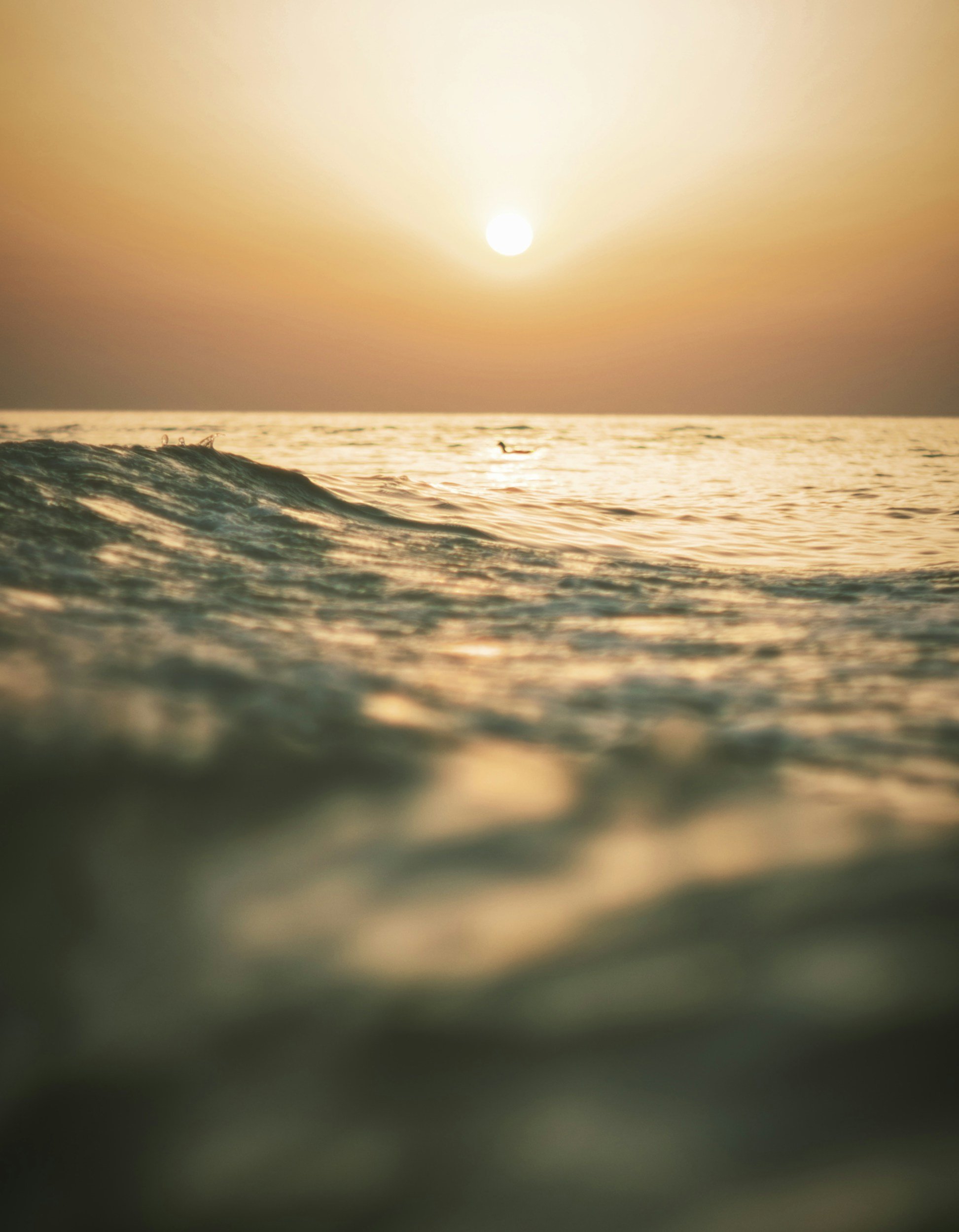Sunset over the ocean with a wave in the foreground and a small boat in the distance.