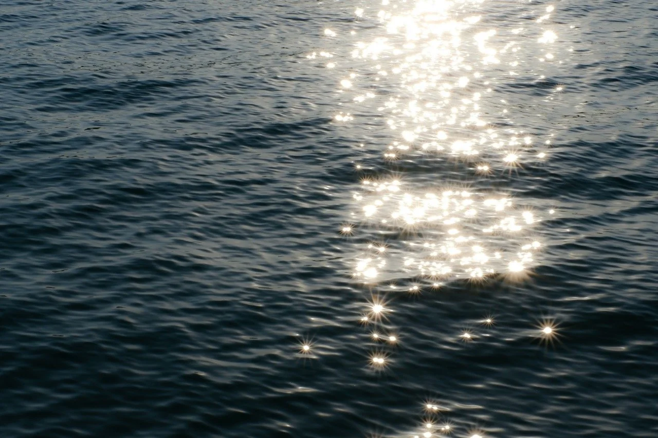 Sunlight reflecting off a calm body of water, creating sparkling light patterns on the surface.