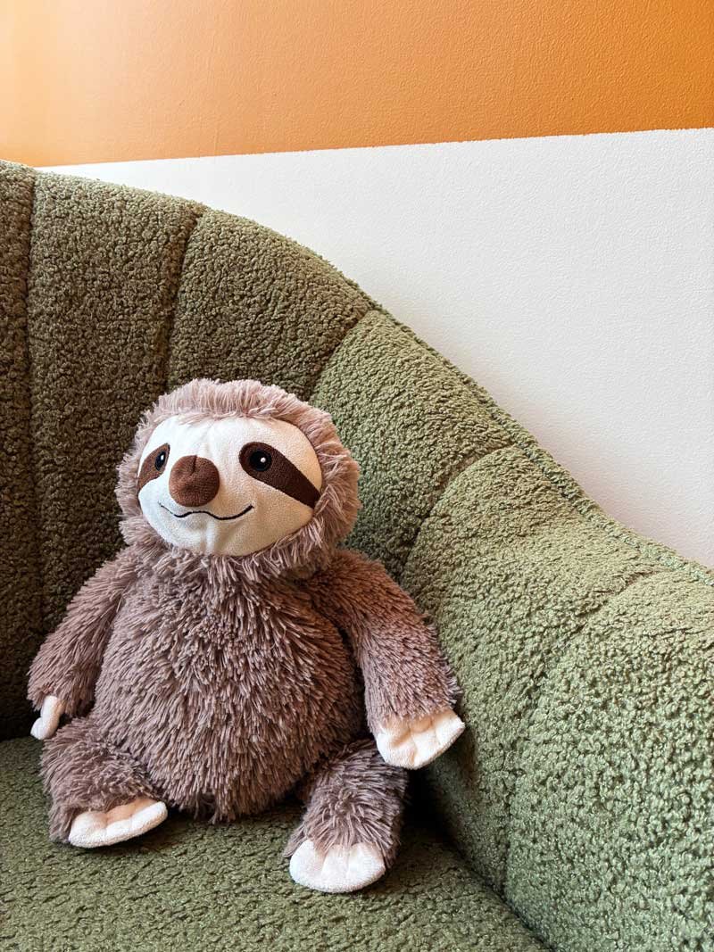 Close up of a sloth stuffed animal on a fuzzy green chair