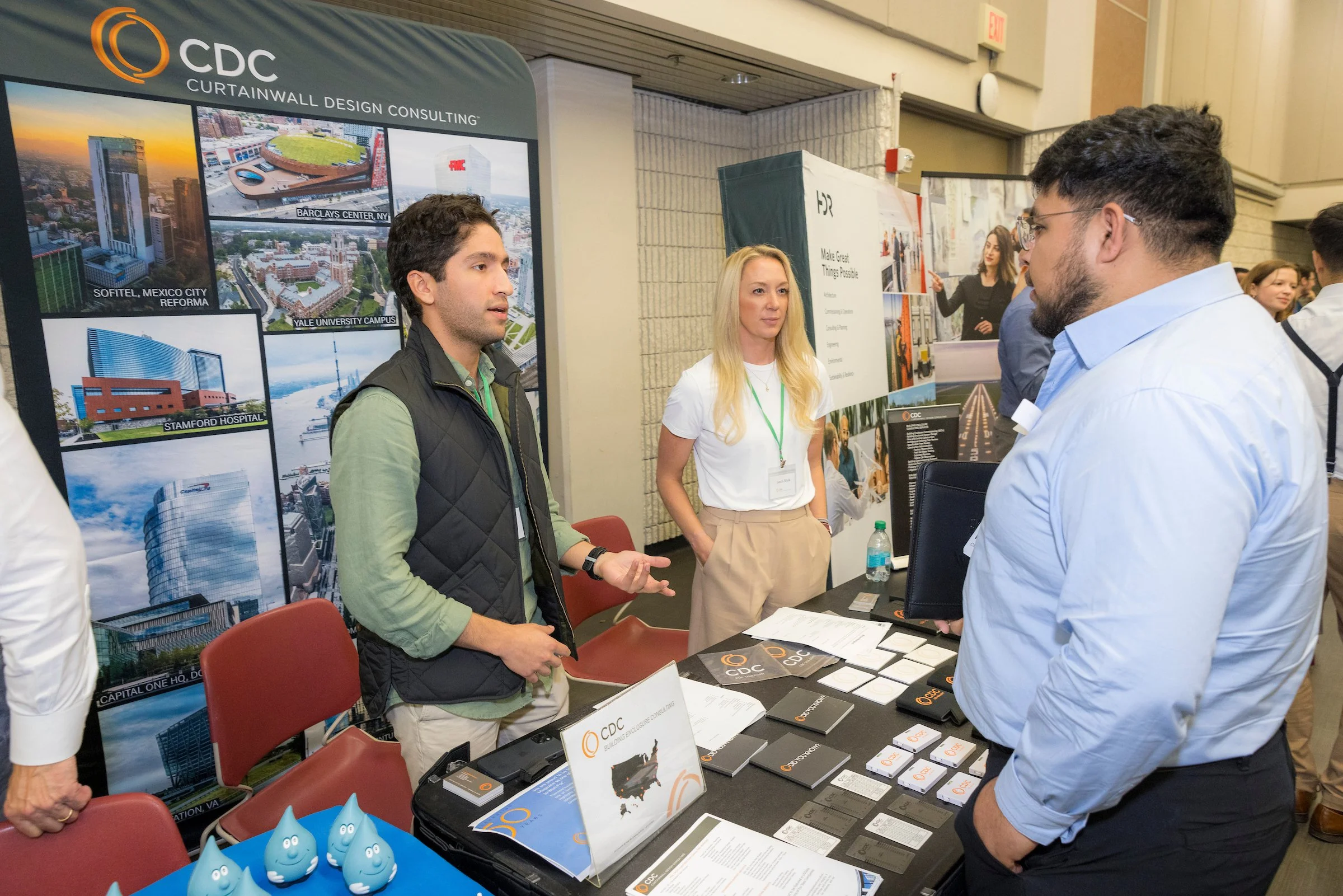 People at a booth discussing architectural projects, with a large CDC banner displaying images of building designs.