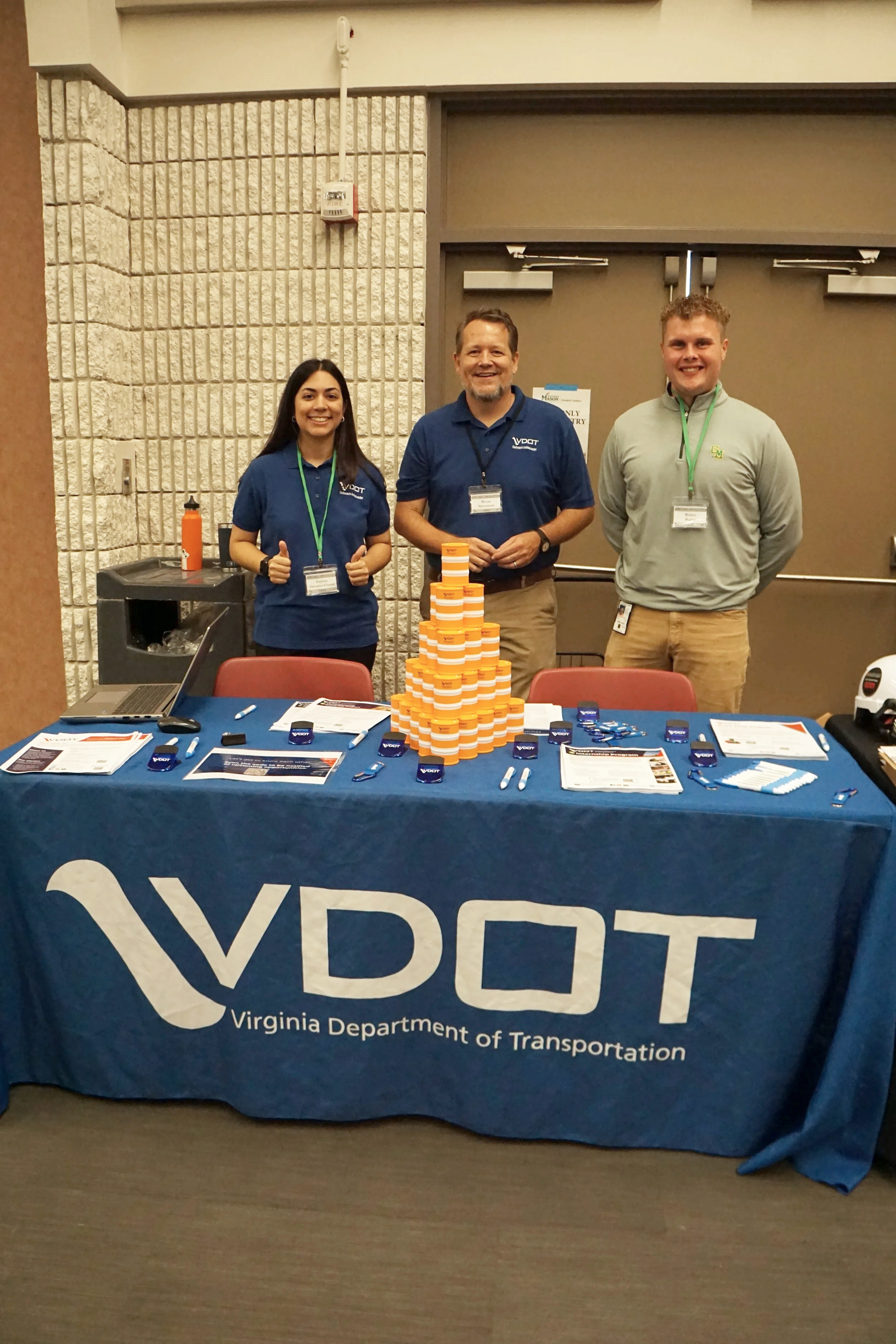 Three people standing behind a Virginia Department of Transportation booth at an event, with a table covered with information and chocolates.