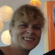 Young woman smiling with curly hair, outdoors with colorful background lights.