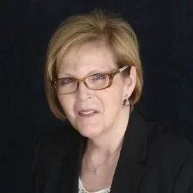 Woman with short blonde hair wearing glasses and a black blazer