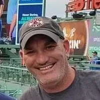 Smiling man wearing a baseball cap outdoors in an urban area