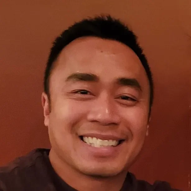 A smiling man with short black hair against a brown background.