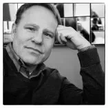Black and white portrait of a man with short hair, smiling slightly, resting his head on his hand.