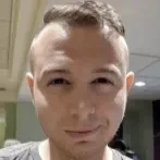 A young man with short hair looking directly at the camera inside a building.
