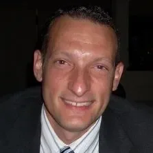 A smiling man with short hair in a dark setting