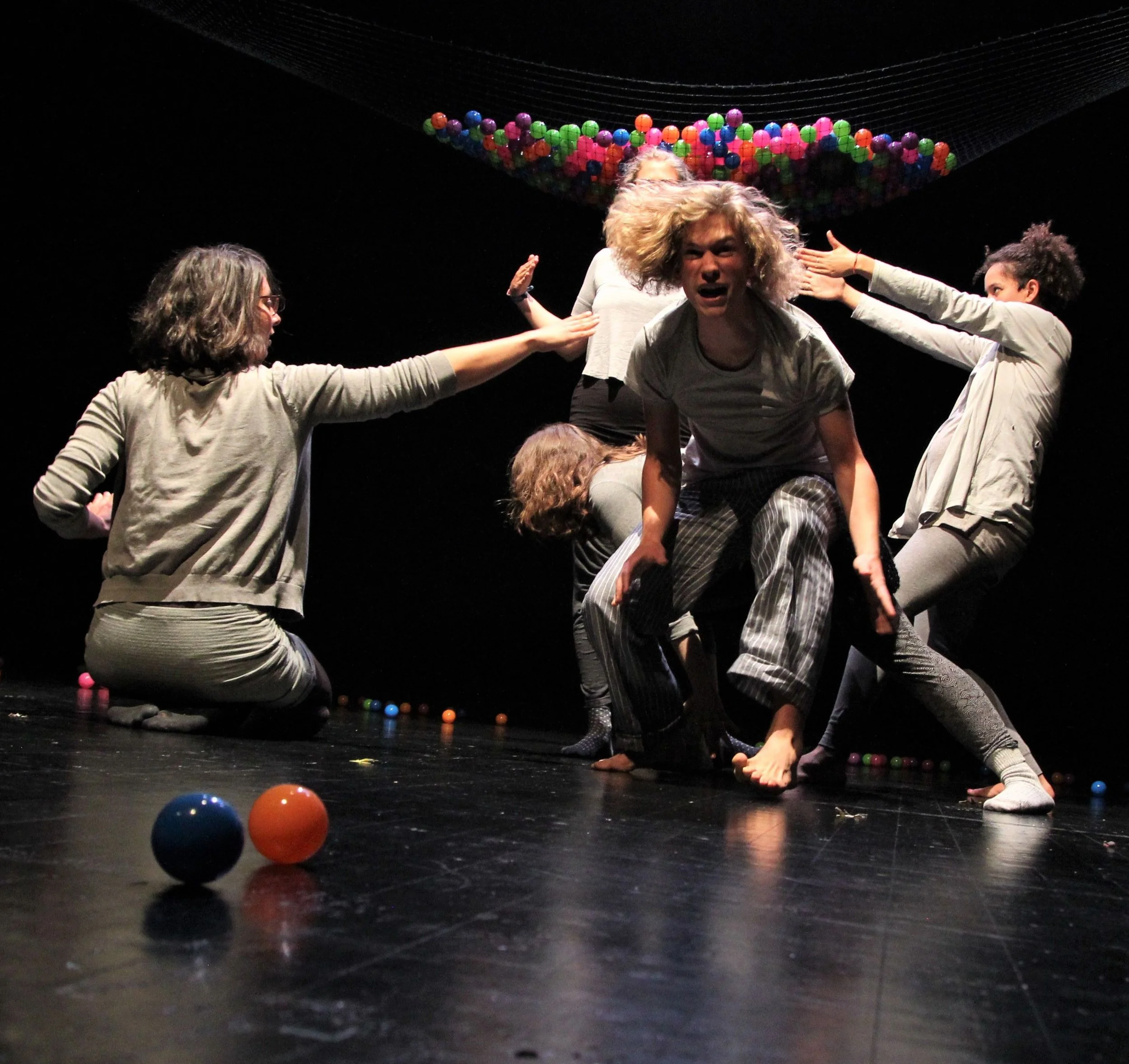 People performing a theatrical or dance scene on stage with colorful balls and a black background.