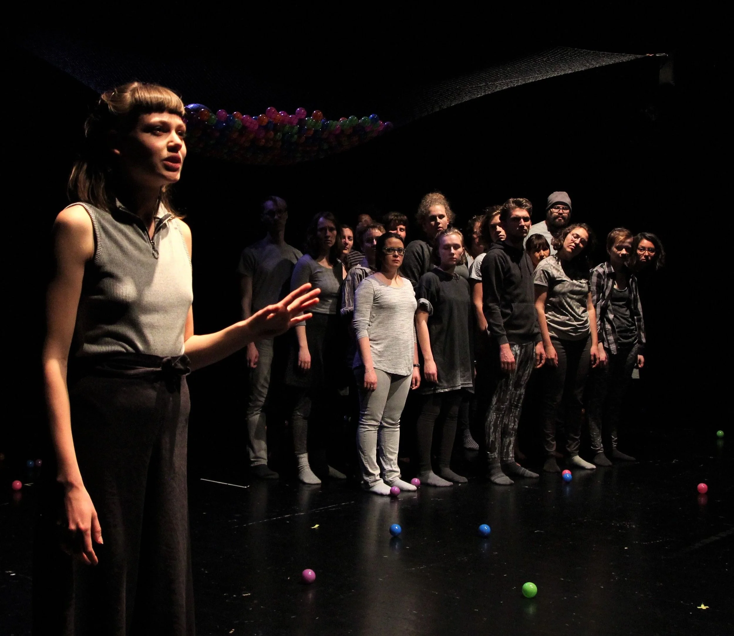 A group of people standing on stage in a dark theater with colorful balls scattered on the floor and hanging from the ceiling.
