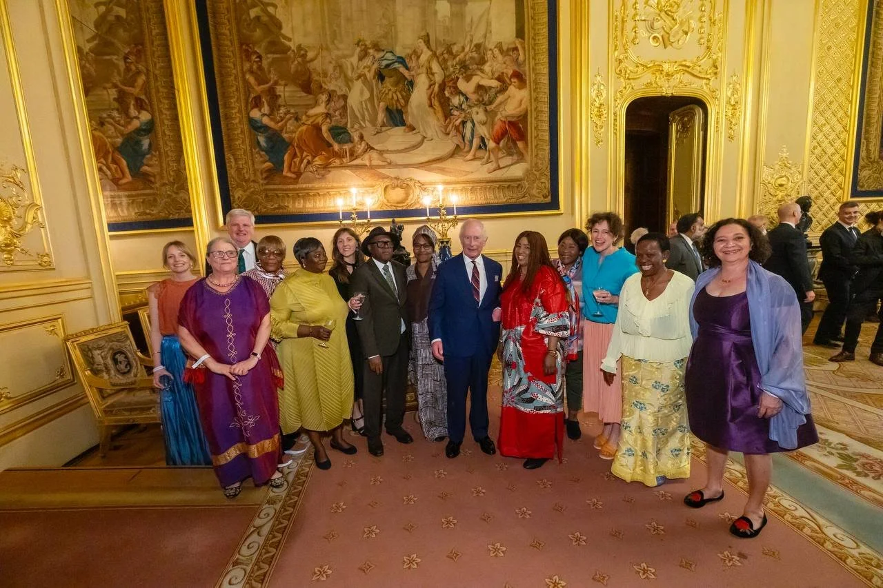 A group of well-dressed people posing for a photo in an ornate, gold-accented room with a large artwork and chandelier overhead.