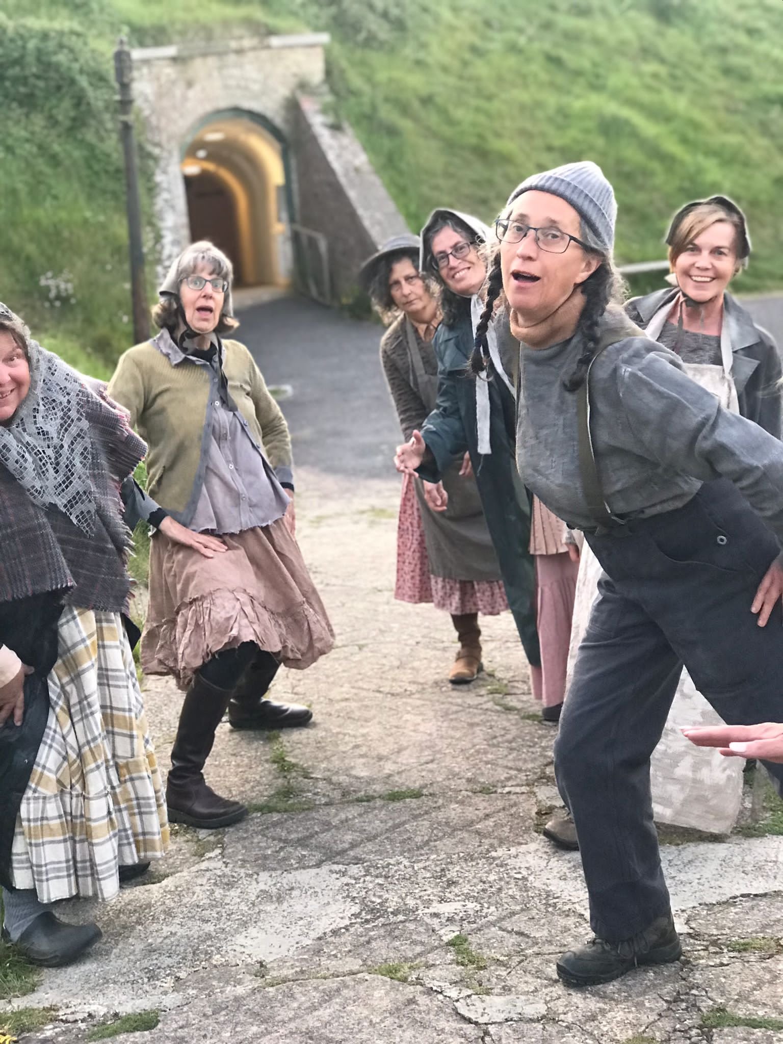 Group of people dressed in vintage clothing standing outdoors near a train tunnel.