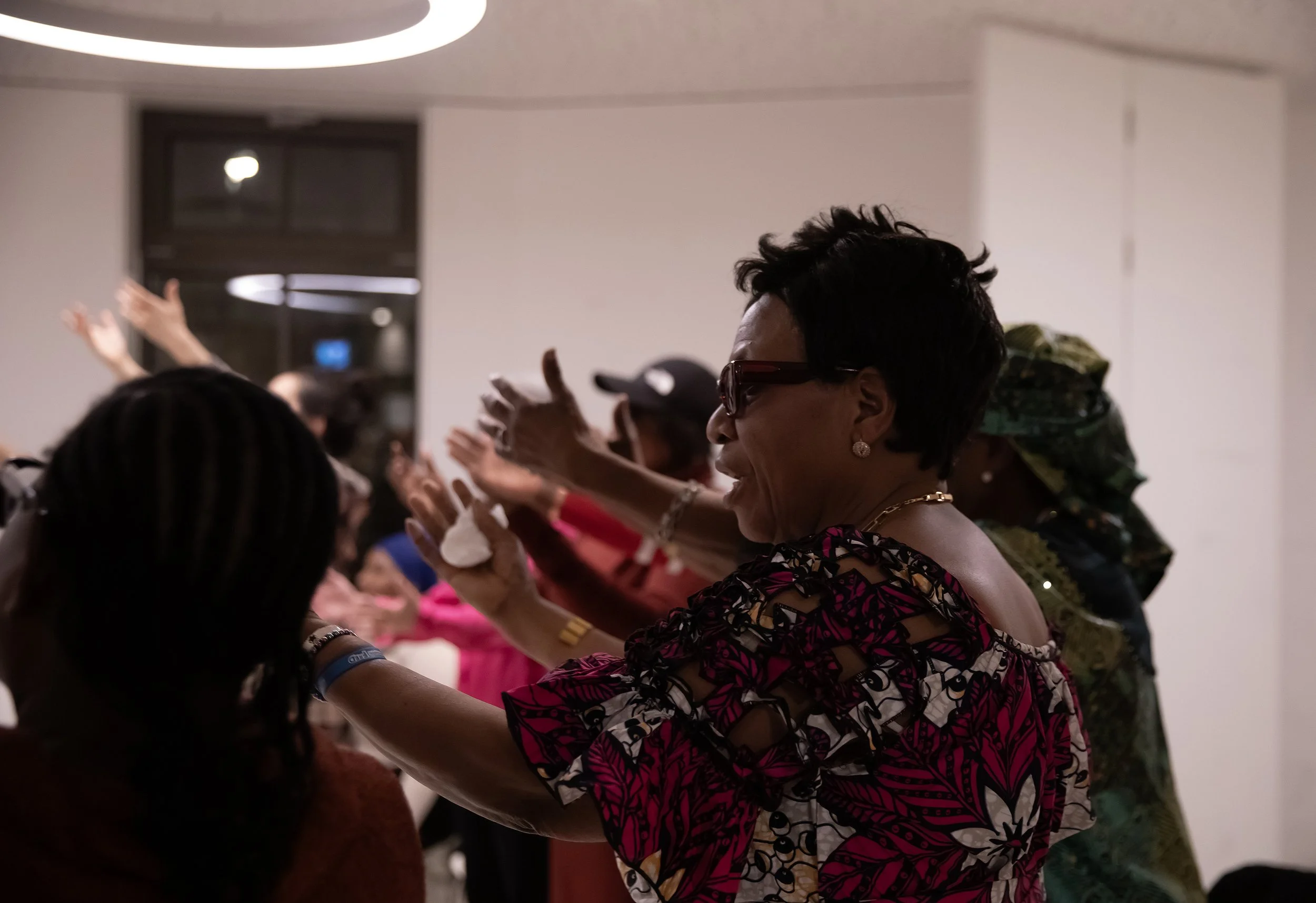 Group of people dancing or celebrating indoors, with some raising their hands, in a lively atmosphere.