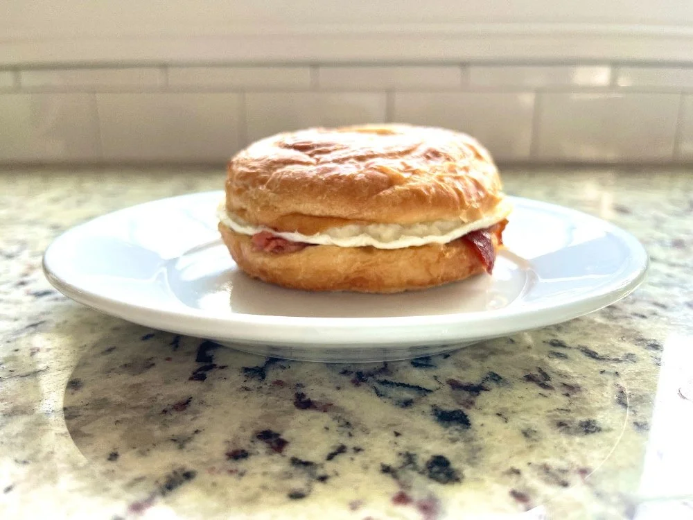 Costco breakfast sandwich with bacon, egg, and cheese on a white plate on a granite countertop