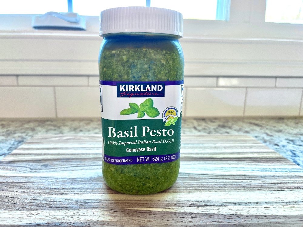 Jar of Kirkland Costco basil pesto on a wooden surface in front of a window