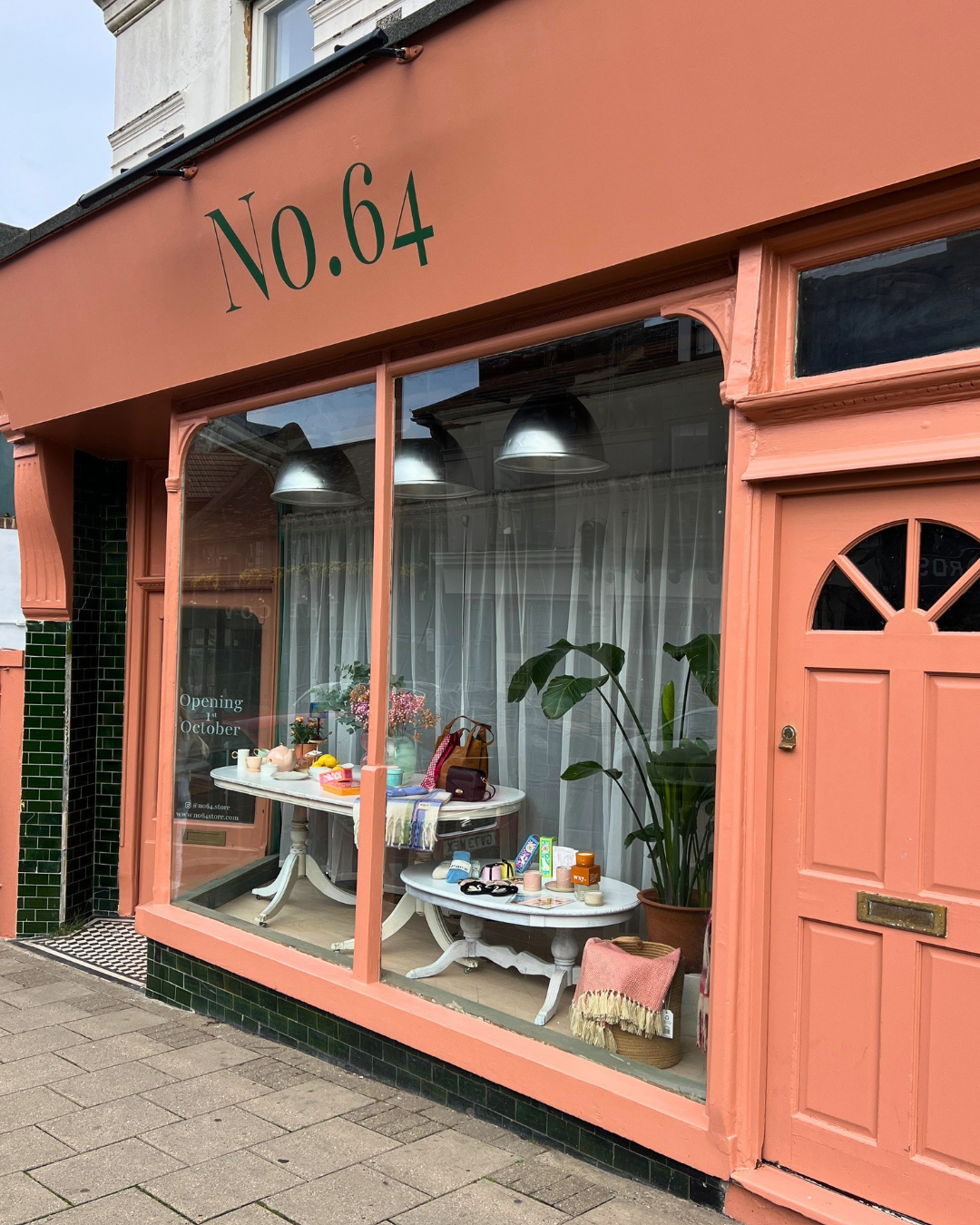 No.64 shopfront on Dyke Road, Seven Dials, with coral-pink facade, "No.64" signage, large display windows showcasing gifts and homeware with fresh plants, and matching coral door