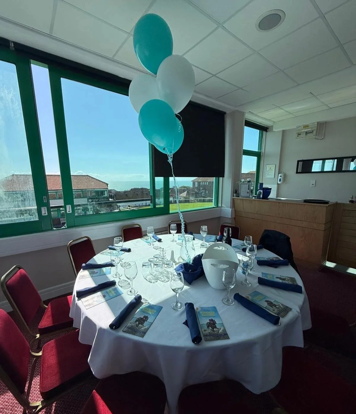 Table set with wine, ice bucket and teal balloons overlooking Brighton Racecourse and the sea