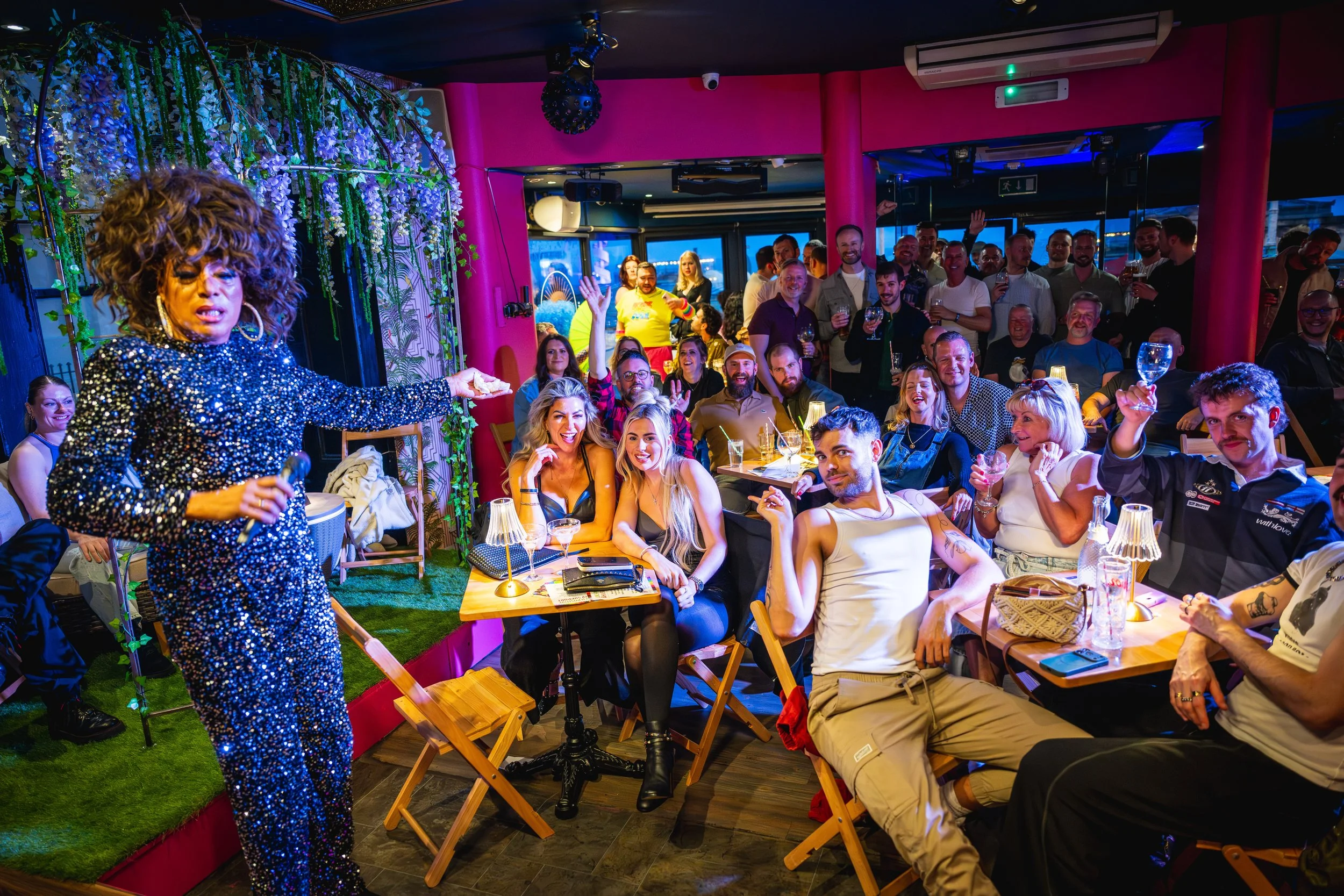 A drag performer entertains a full room of seated and standing guests at The Birdcage in Kemptown, Brighton