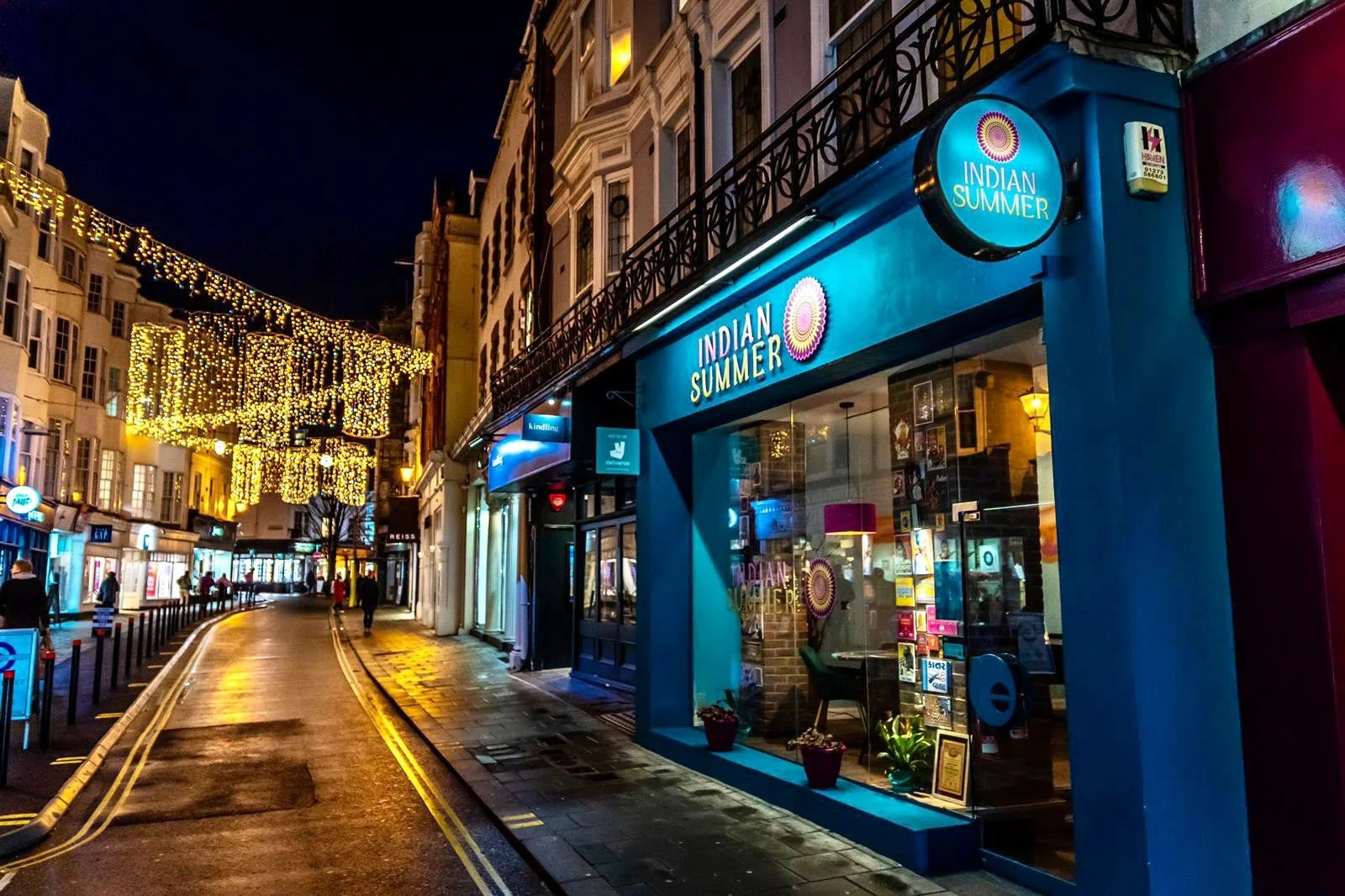 The blue frontage of Indian Summer restaurant on East Street in Brighton at night with festive lights above the street