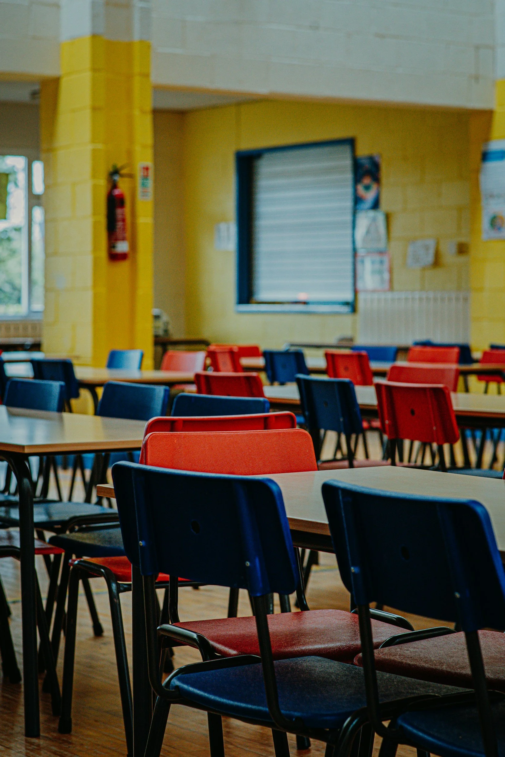 An empty school classroom with rows of desks and red and blue chairs