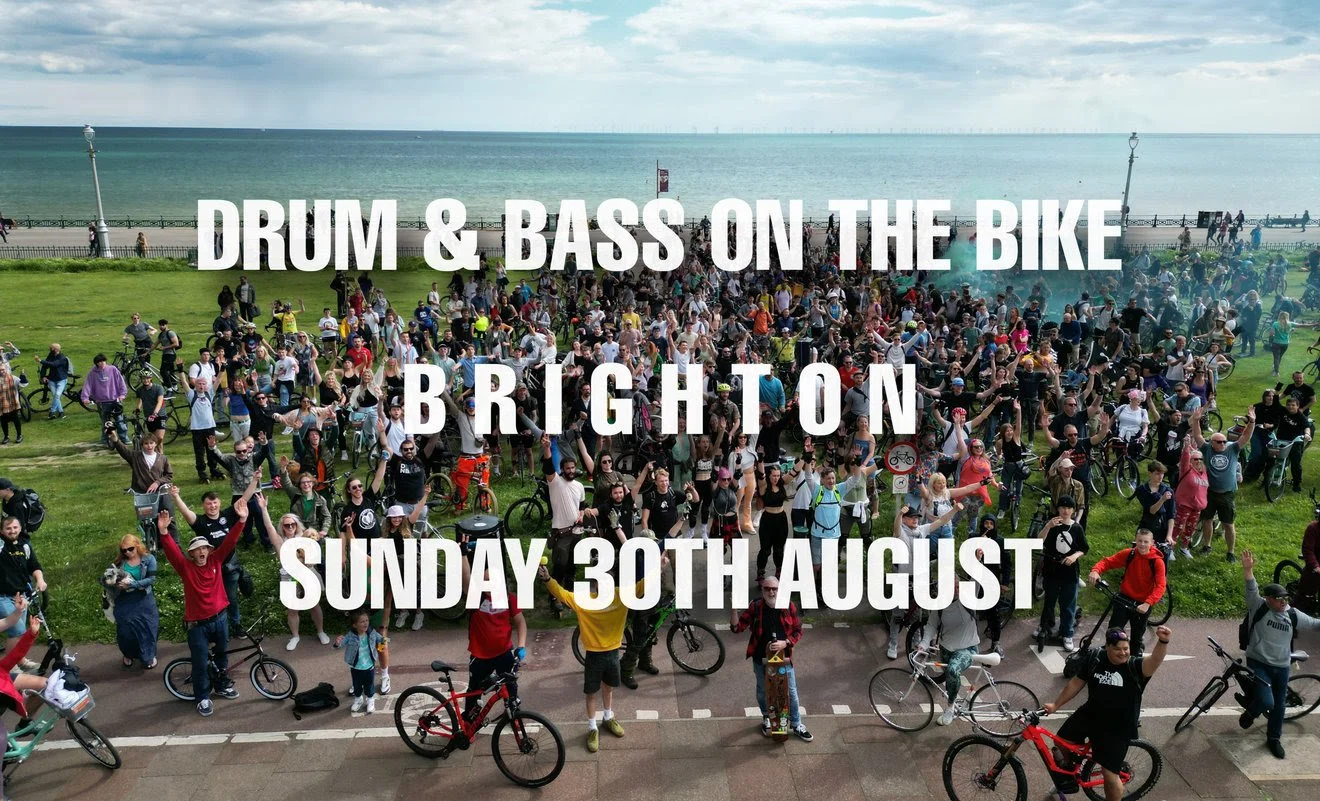 Hundreds of cyclists with arms raised on Brighton seafront lawns for Drum & Bass On The Bike under a Sunday 30th August banner