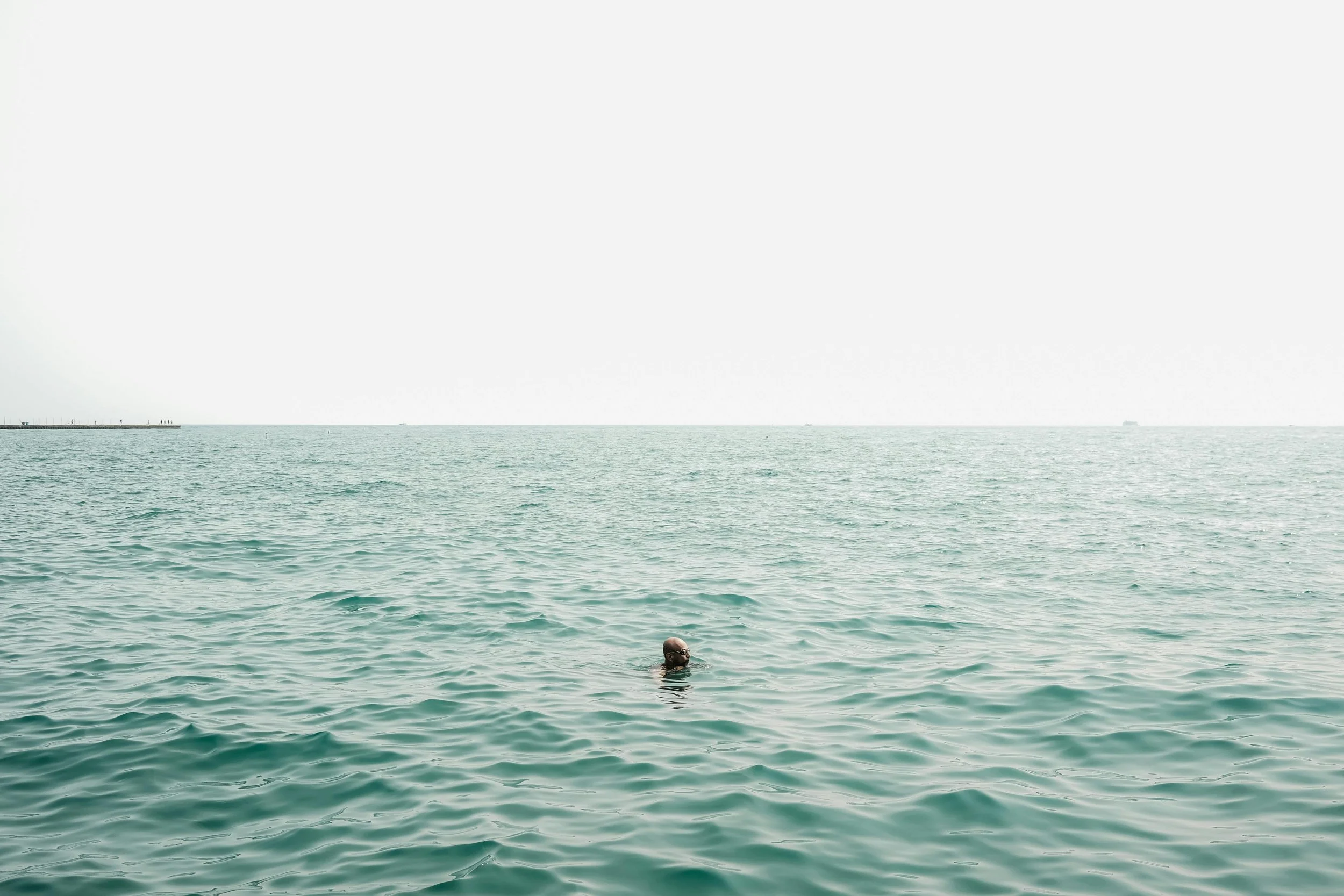 A swimmer in calm green open water with a pier in the distance