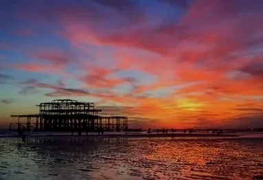 Brighton West Pier silhouetted against a dramatic orange pink and purple sunset sky reflected in the sea