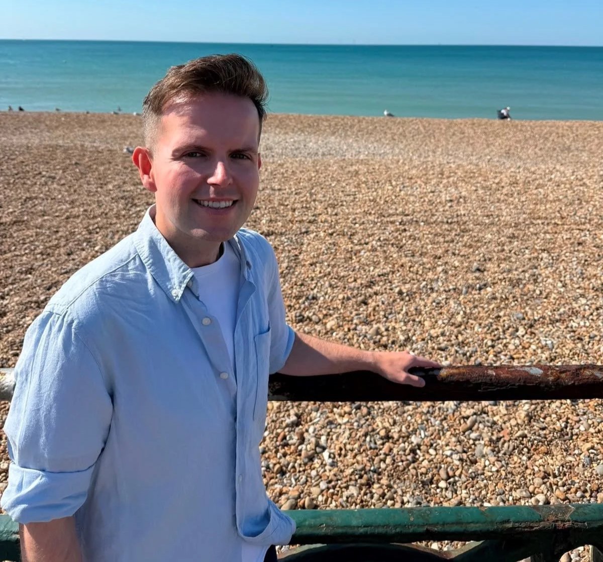 Man beside the historic cast iron seafront railings on Hove seafront, with the beach and sea behind