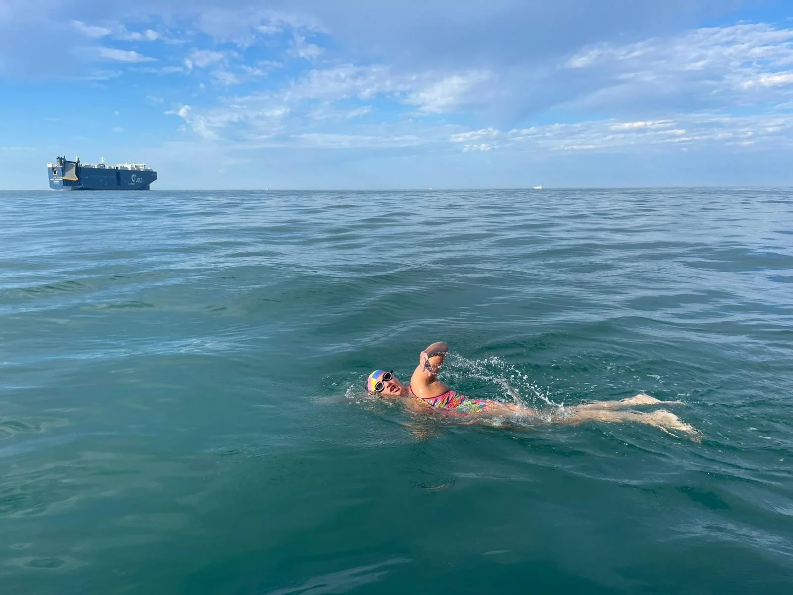 Melanie Barratt swimming front crawl in open water with a cargo ship on the horizon