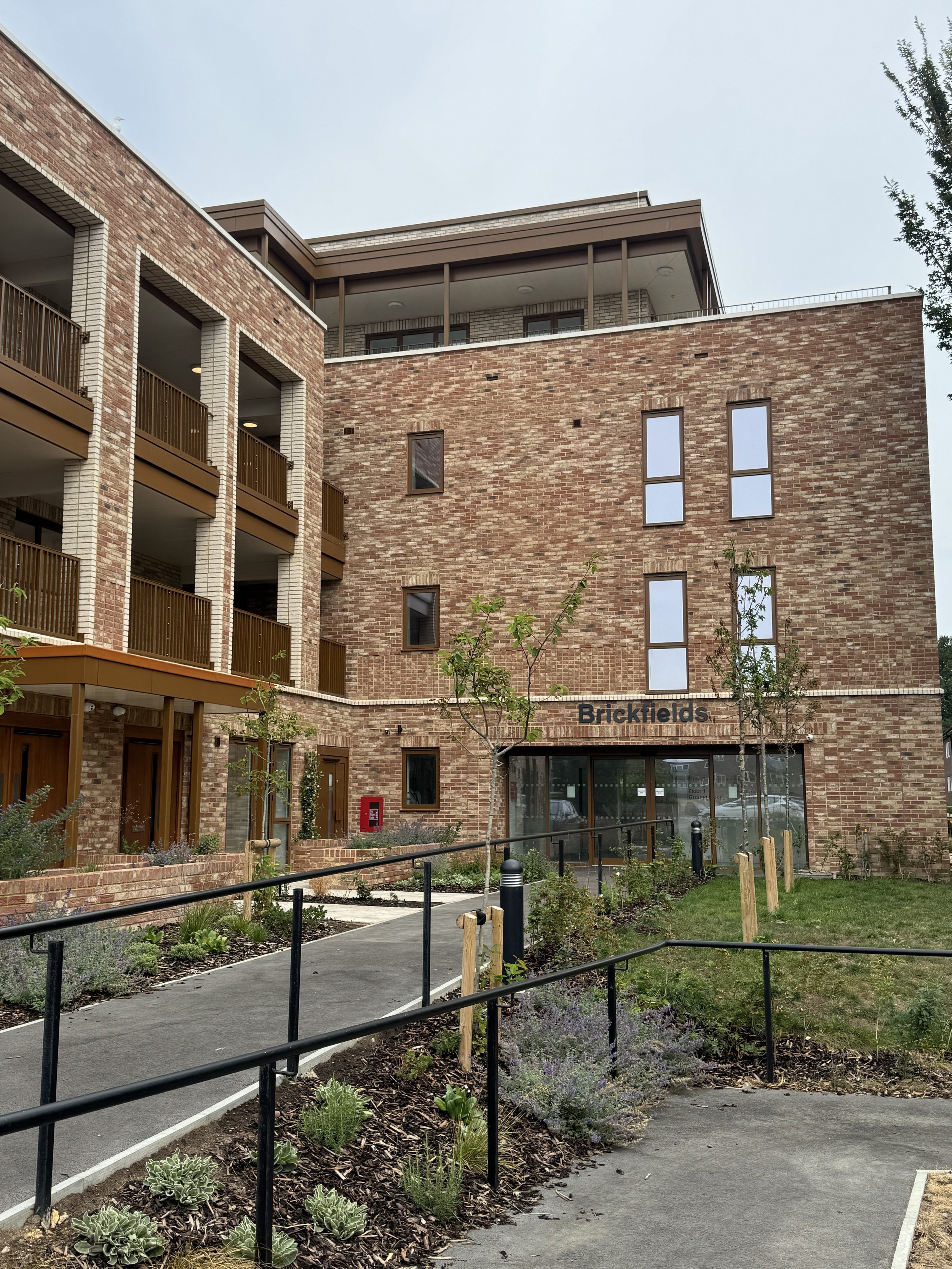 The entrance of the completed Brickfields supported living building in Hove, with Brickfields signage, brick facade, balconies and an accessible ramp with handrails