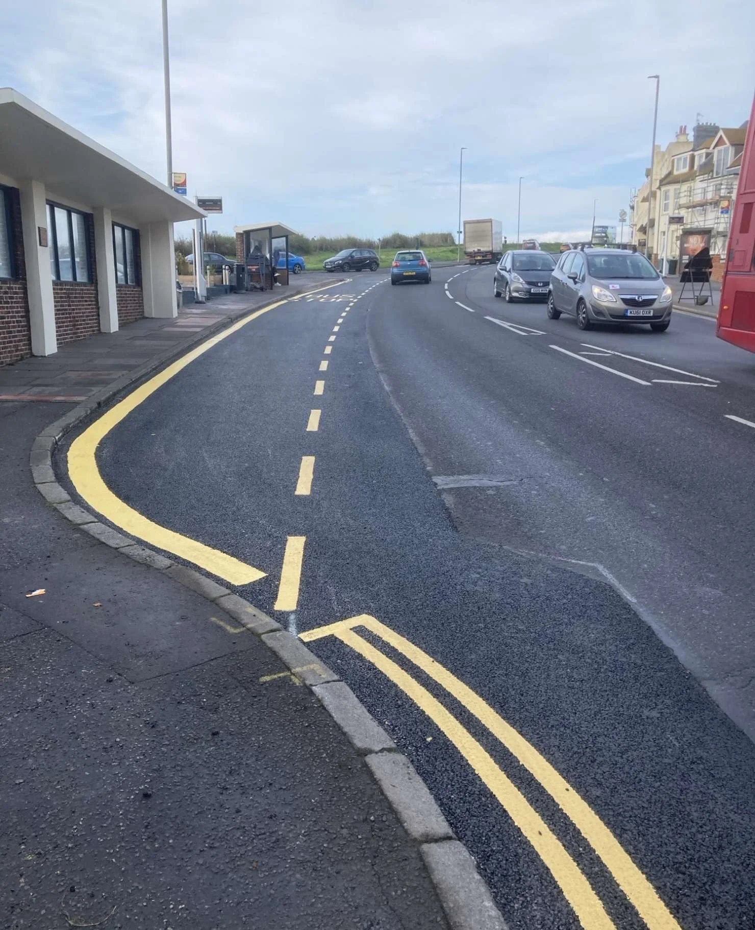Freshly painted yellow bus stop markings and double yellow lines on a Brighton dual carriageway near the seafront, with traffic and a bus visible