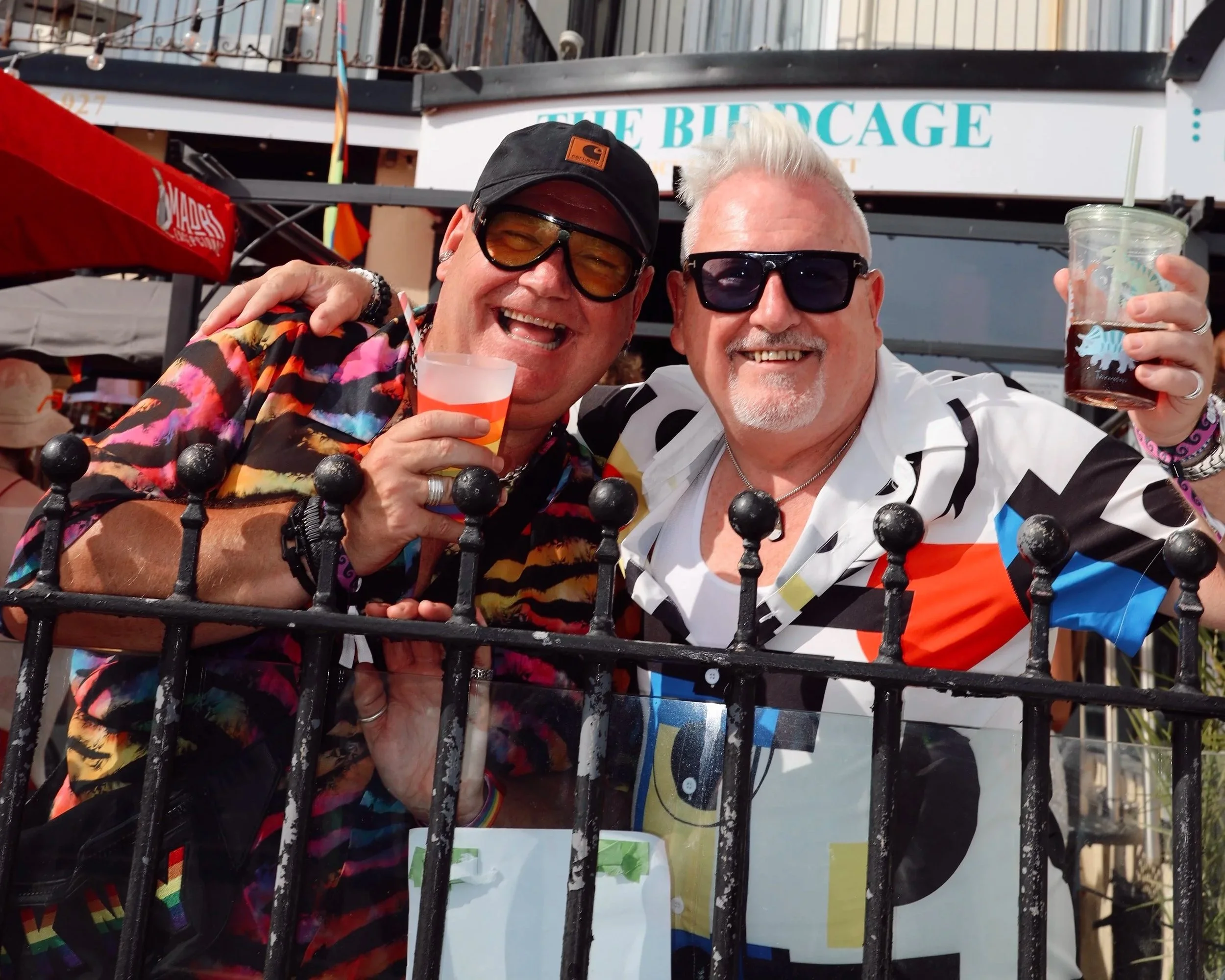 Two guests celebrating outside The Birdcage in Kemptown, Brighton, with a Pride flag visible on the balcony above