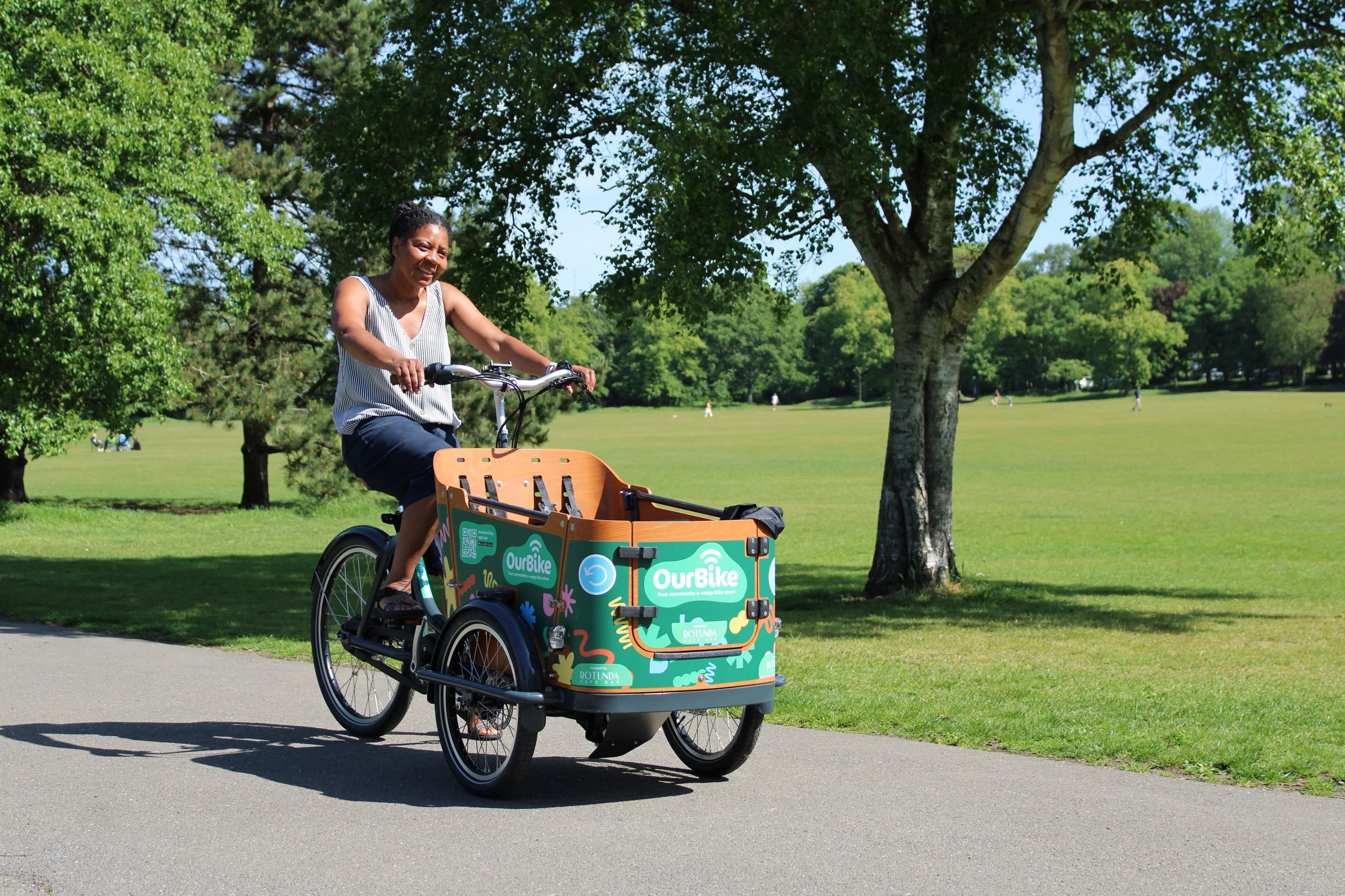 Woman riding an OurBike electric cargo bike through a Brighton park