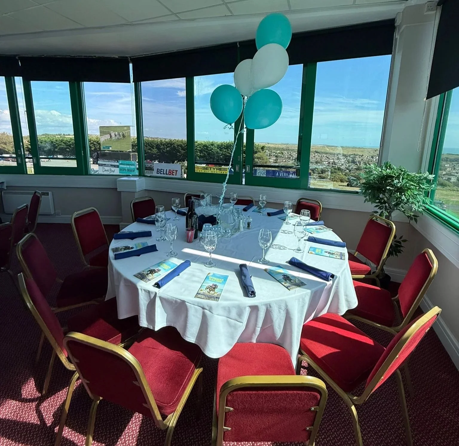 Dinner table set beneath balloons with floor-to-ceiling windows overlooking Brighton Racecourse and the seaDinner table set beneath balloons with floor-to-ceiling windows overlooking Brighton Racecourse and the sea