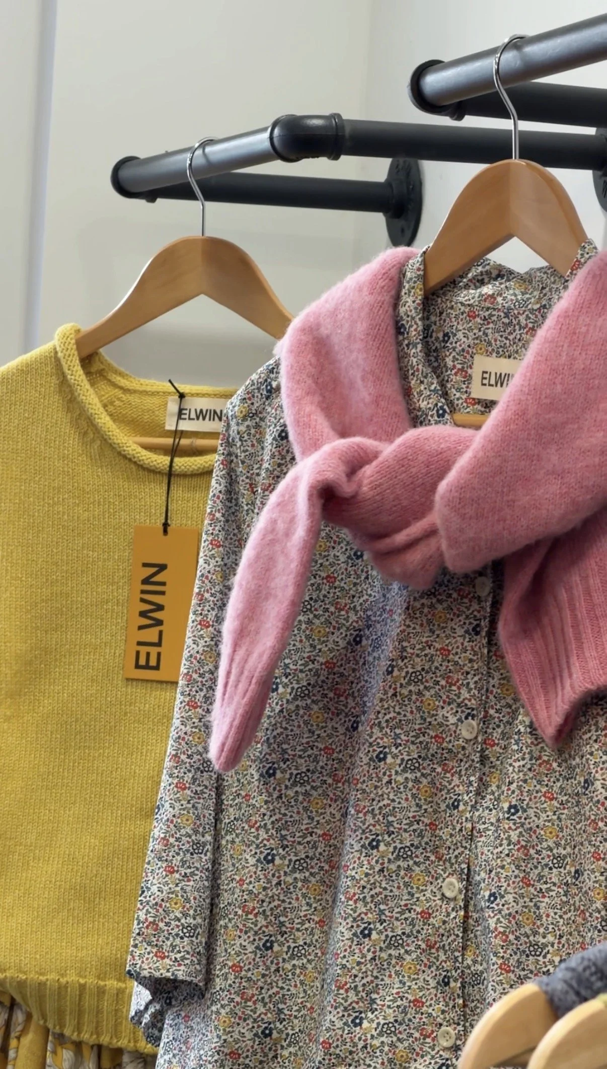 ELWIN yellow knit and floral pieces on a rail with orange ELWIN swing tags