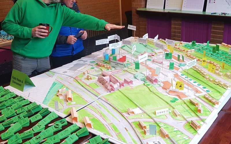 Residents looking at a large 3D model of the Moulsecoomb neighbourhood covered in coloured cards and flags during a Planning for Real session