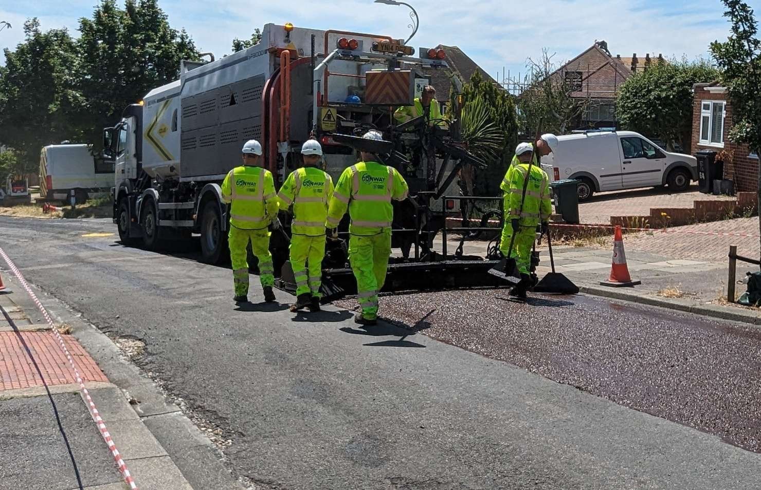 A road maintenance crew from Conway in high-visibility clothing operating a paving machine to lay new road surface material on a Brighton residential street