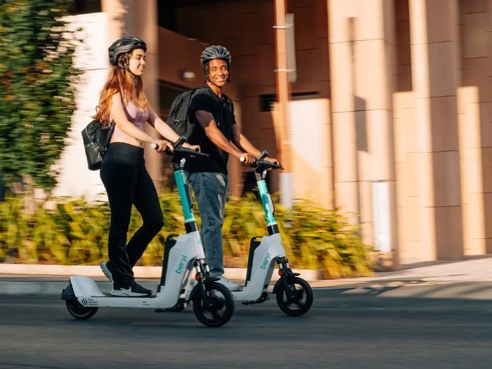 Two people riding Beryl e-scooters through Brighton