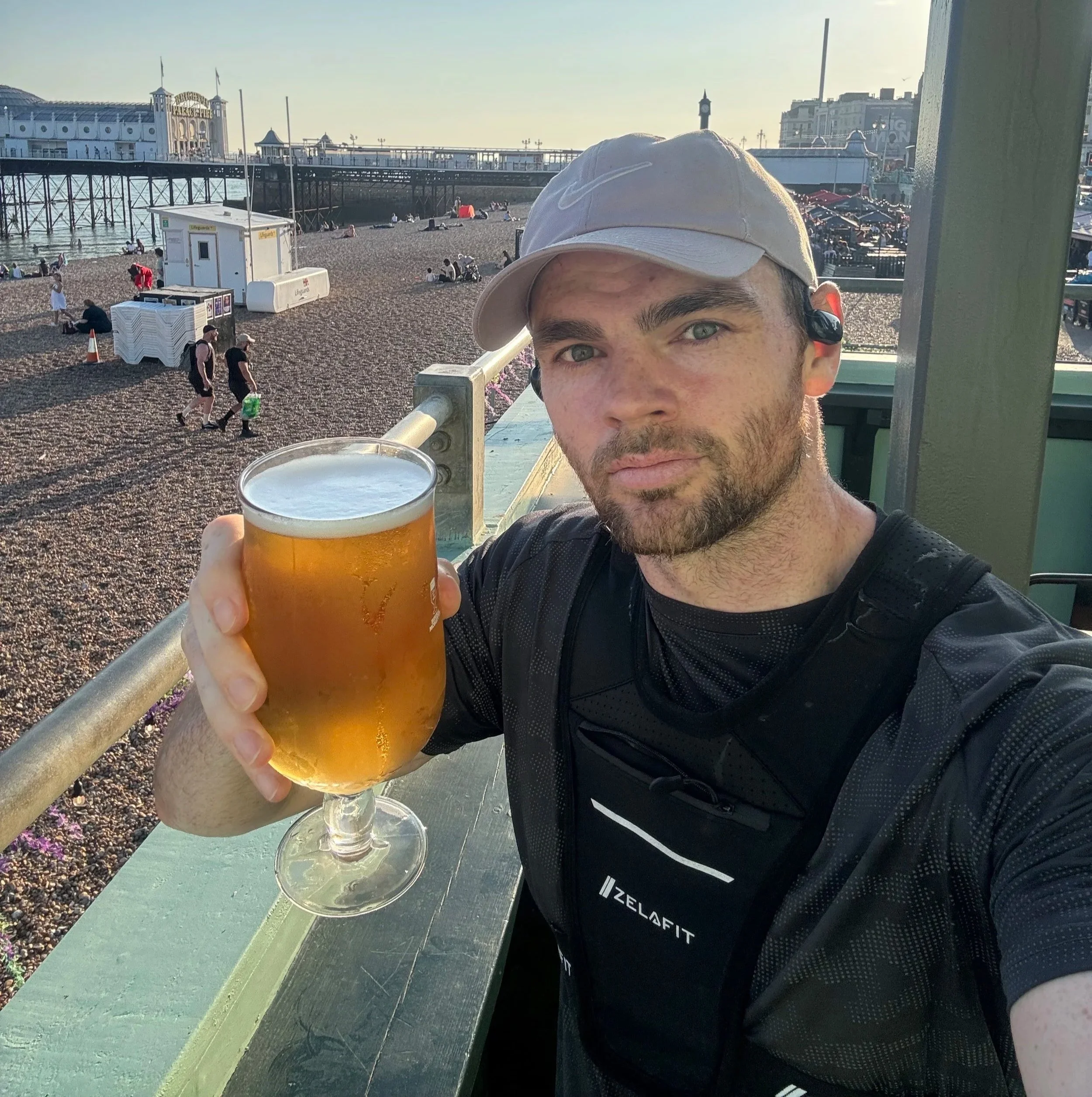 Declan O'Sullivan holding a pint after a TA Fitness Run Club social run on Brighton seafront with Brighton Palace Pier in the background.