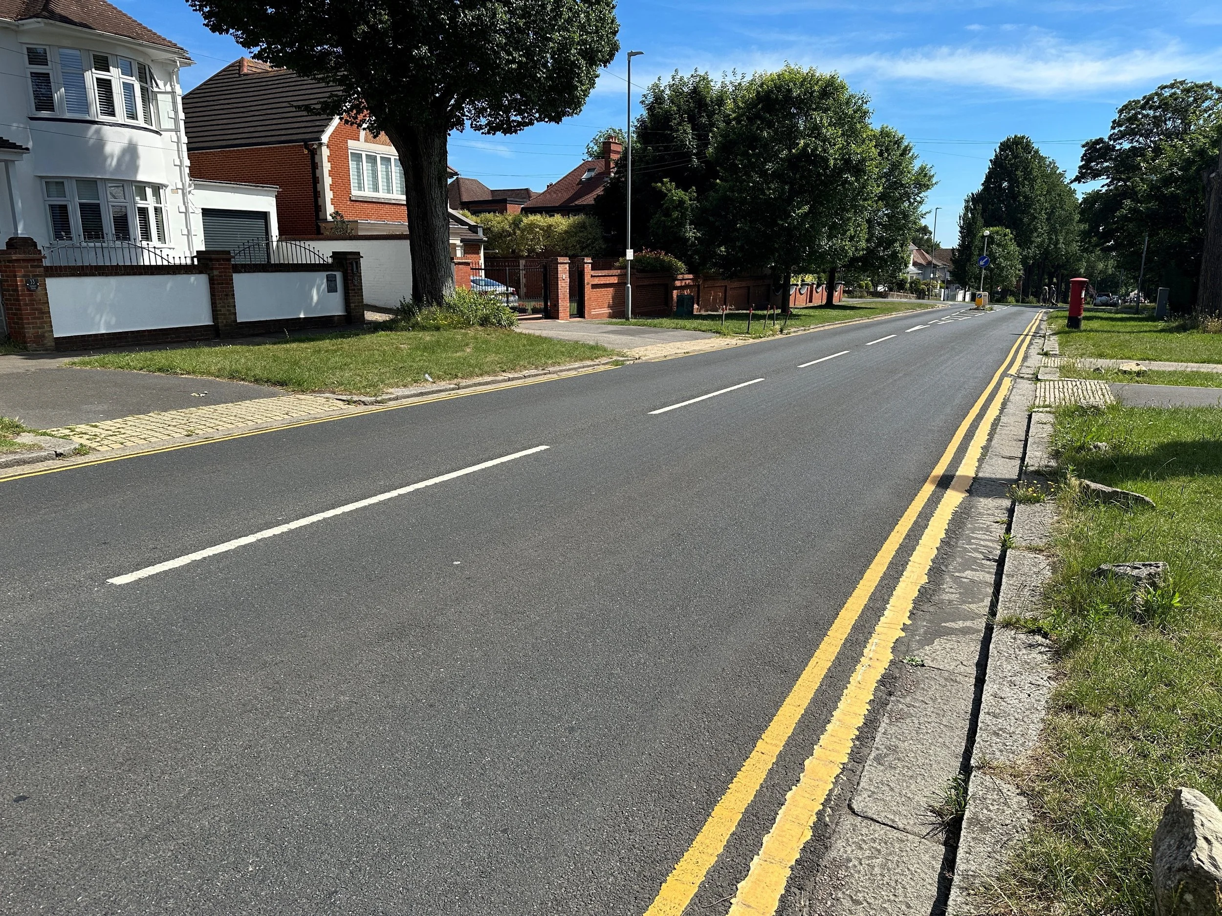A newly resurfaced residential Brighton street with fresh double yellow lines and white road markings, tree-lined with large houses either side