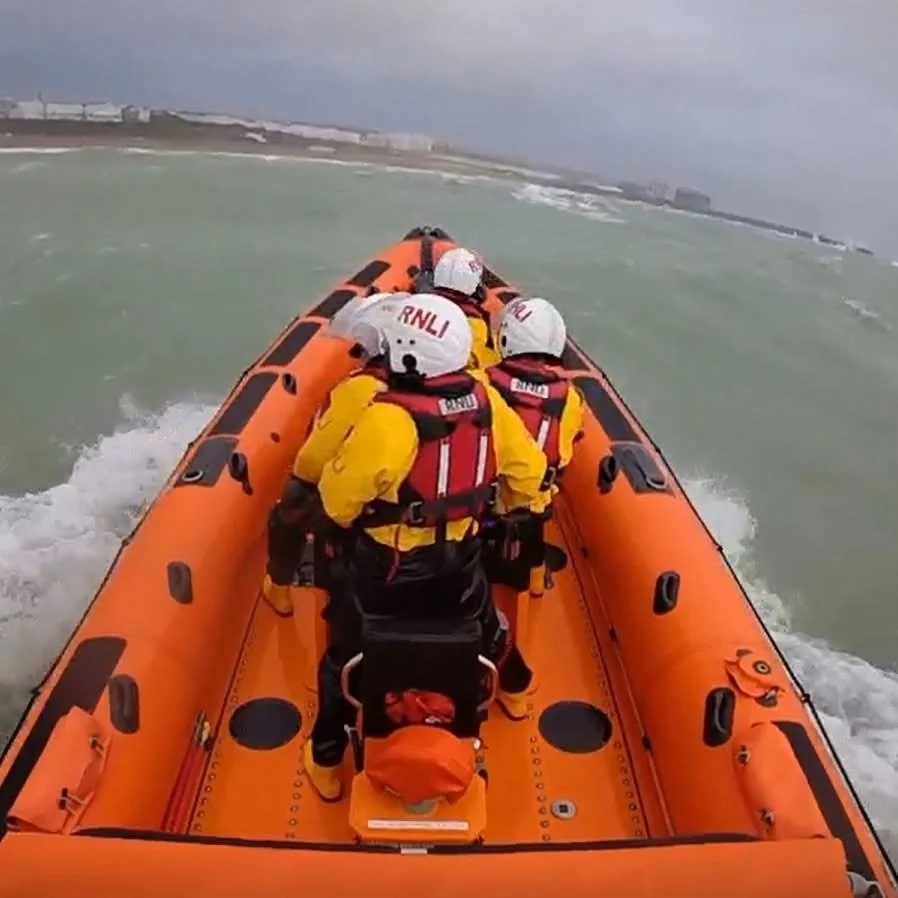 Brighton RNLI volunteer crew in an orange inshore lifeboat heading through rough grey green sea towards the Brighton coast