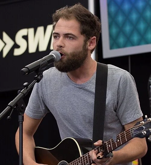 Passenger, Mike Rosenberg, singing into a microphone and playing acoustic guitar during a live performance