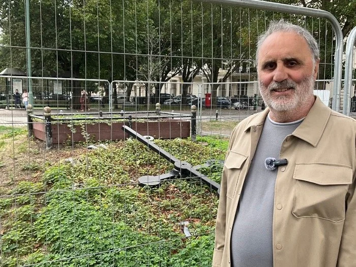 Man standing in front of the fenced-off derelict Floral Clock mound at Palmeira Square showing overgrown vegetation and deteriorated infrastructure