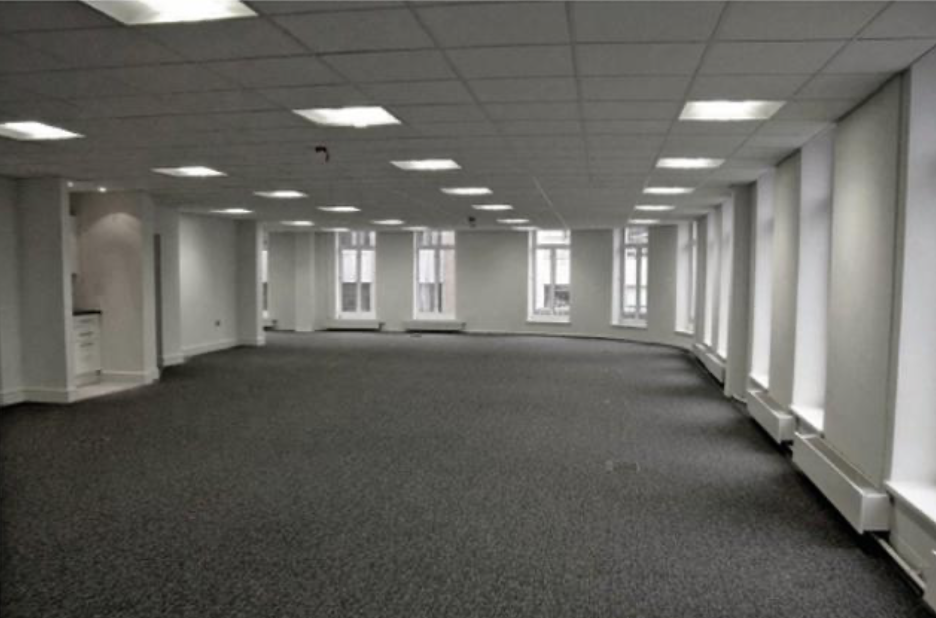 An empty open-plan office floor with grey carpet and large windows inside one of the council buildings