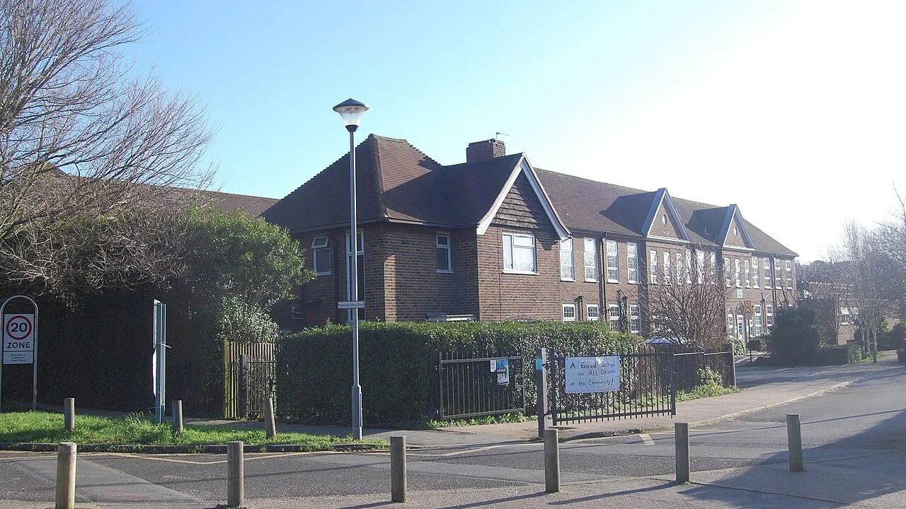 The red brick Moulsecoomb Primary School on Moulsecoomb Way, Brighton, with a banner on the gate reading A Good School for All Children in this Community