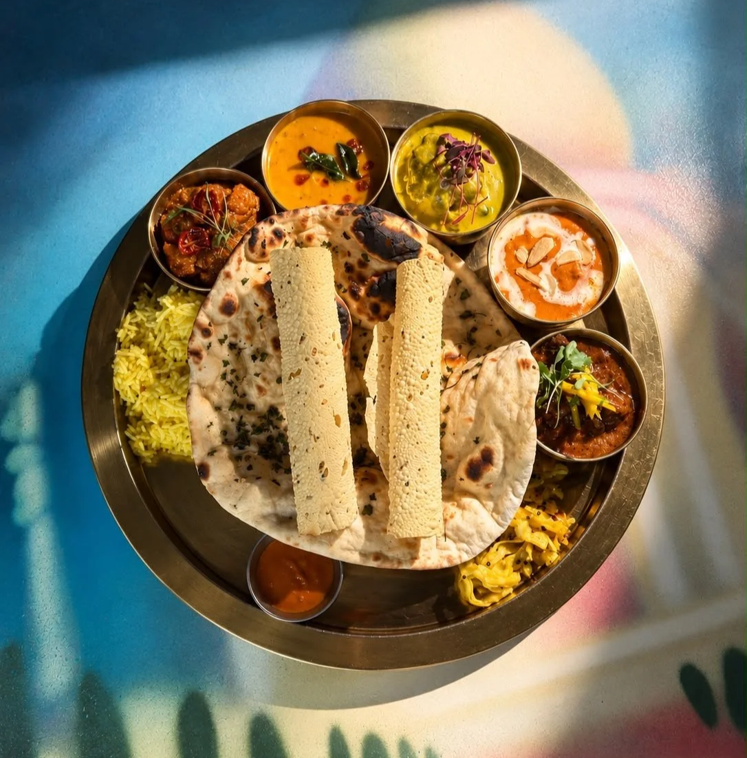 Overhead view of an Indian Summer thali on a brass tray with naan, papads, rice and bowls of curry in Brighton
